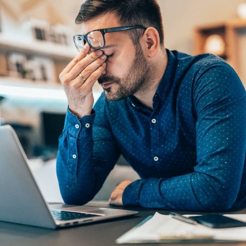 Tired young businessman working at home using lap top and looking Anxious
